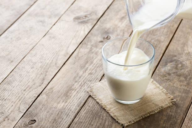 milk pouring from jug into glass on old wooden table