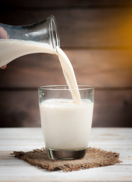 Milk from a jug pouring into glass on wooden,morning light